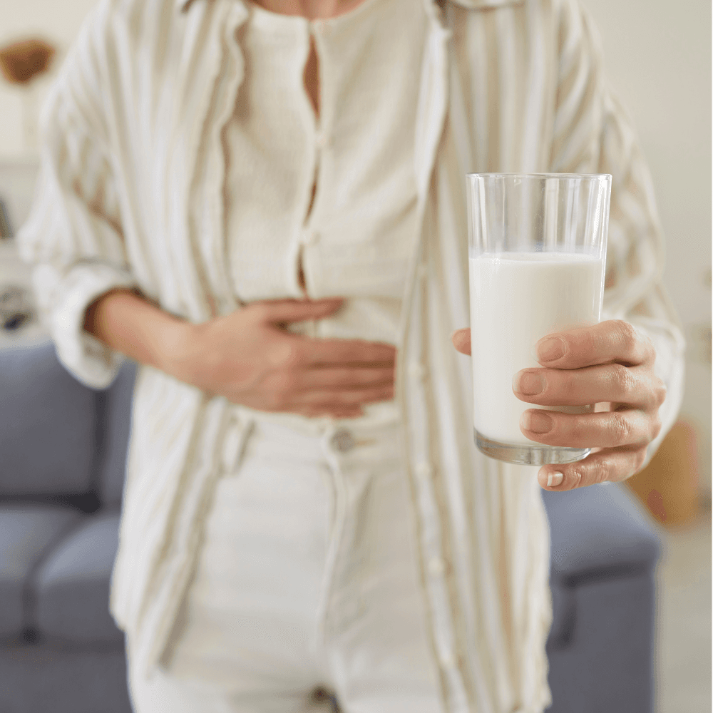 Eine Frau hält sich den Bauch und hält ein Glas Milch in der Hand