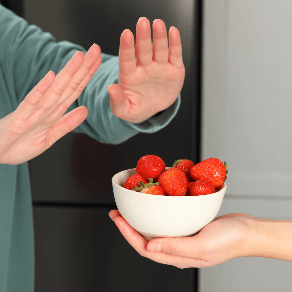 Ablehnende Hände gegenüber einer Schale Erdbeeren