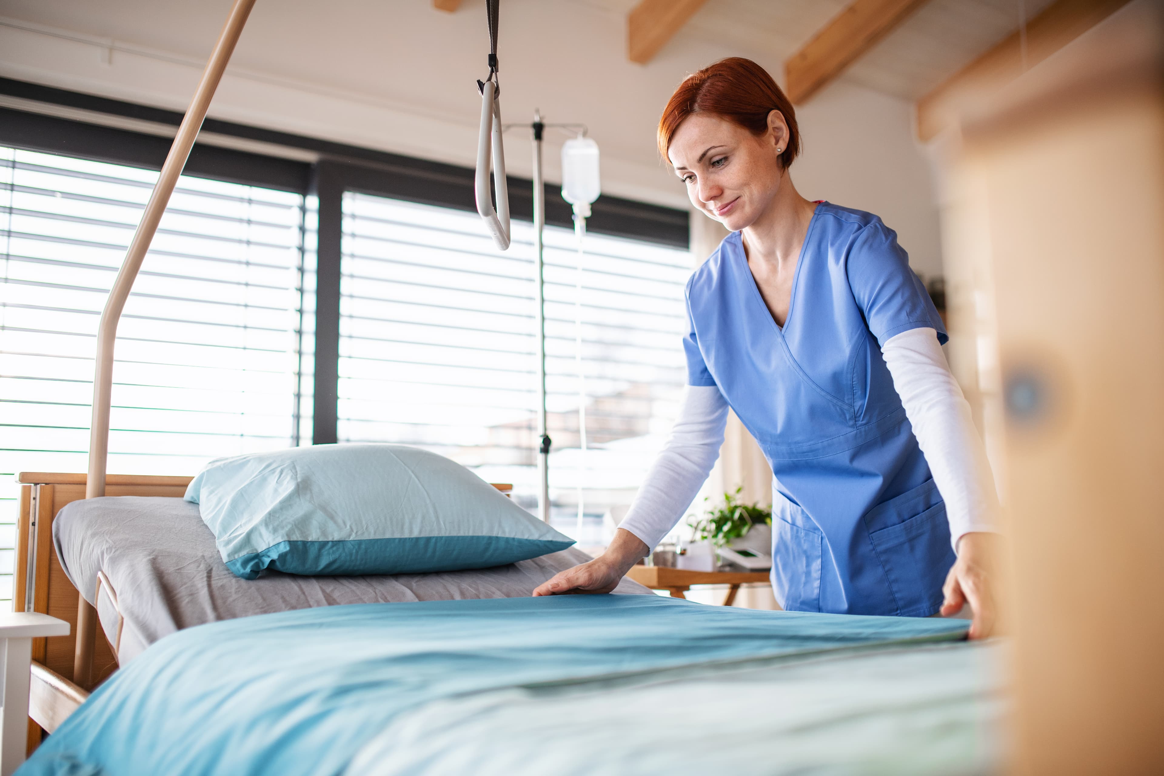 Pflegekraft macht ein Krankenbett in einem hellen Patientenzimmer.