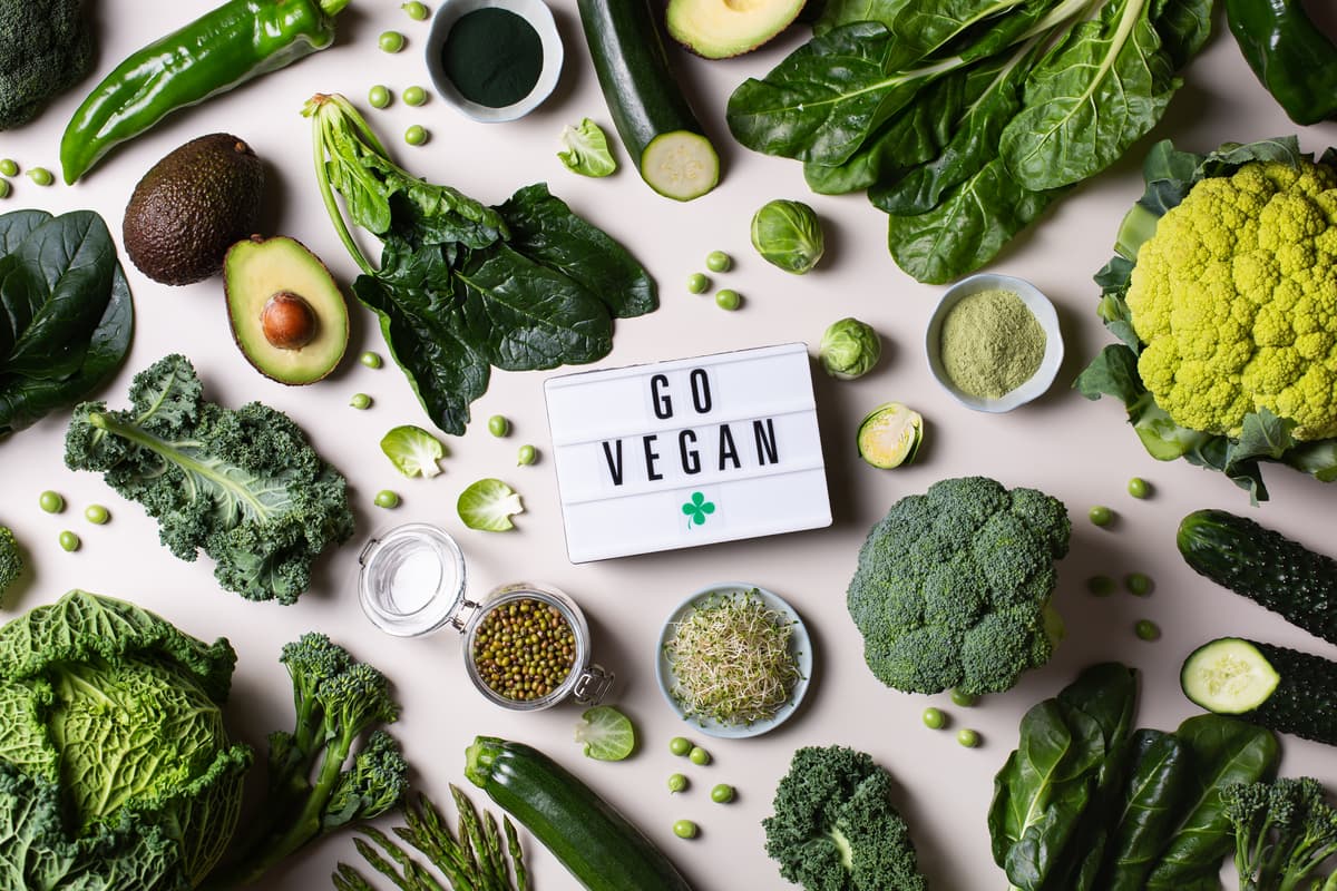 Verschiedene grüne Gemüsesorten und Samen um ein Schild mit der Aufschrift „Go Vegan“ arrangiert.