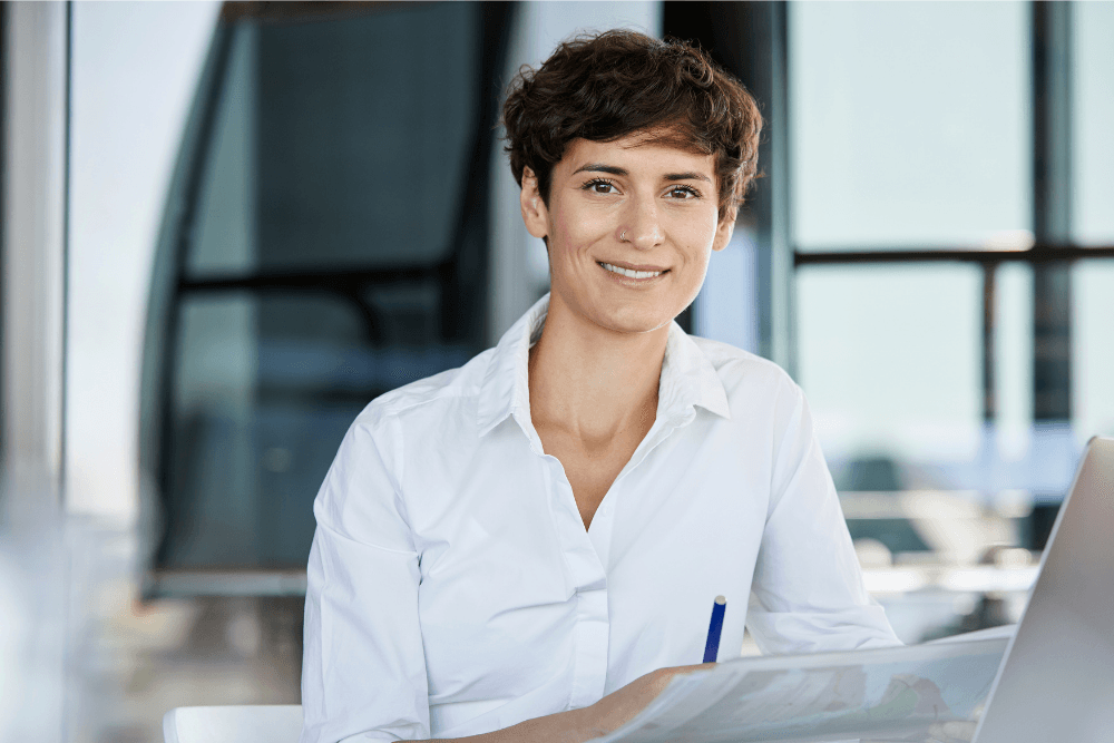 Lächelnde Frau arbeitet mit Laptop und Unterlagen im modernen Büro.