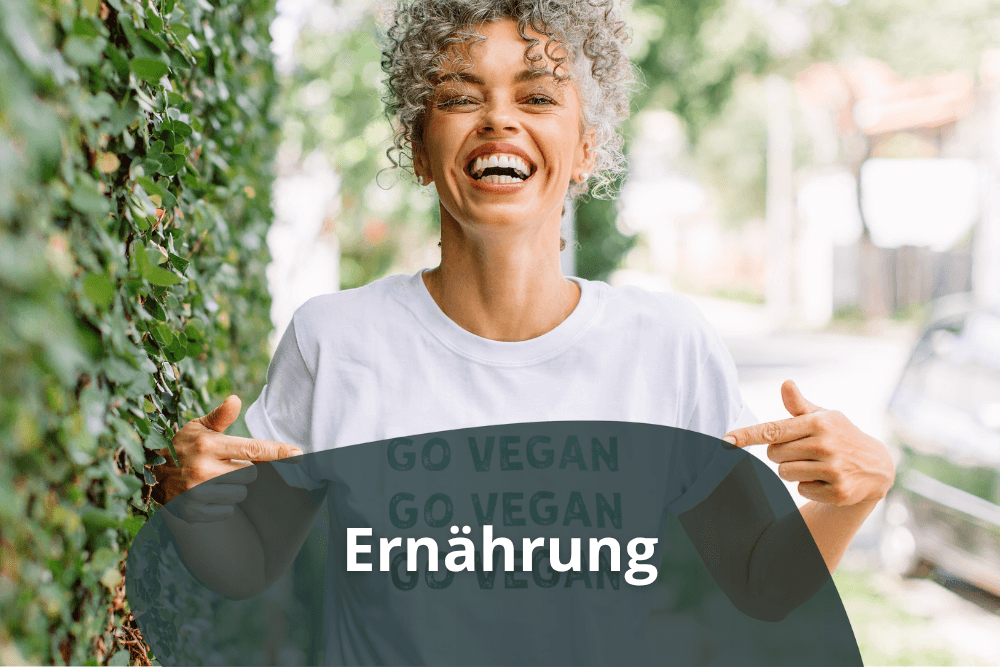 Eine lachende Frau zeigt auf ein Tshit Schriftzug mit veganer Ernährung
