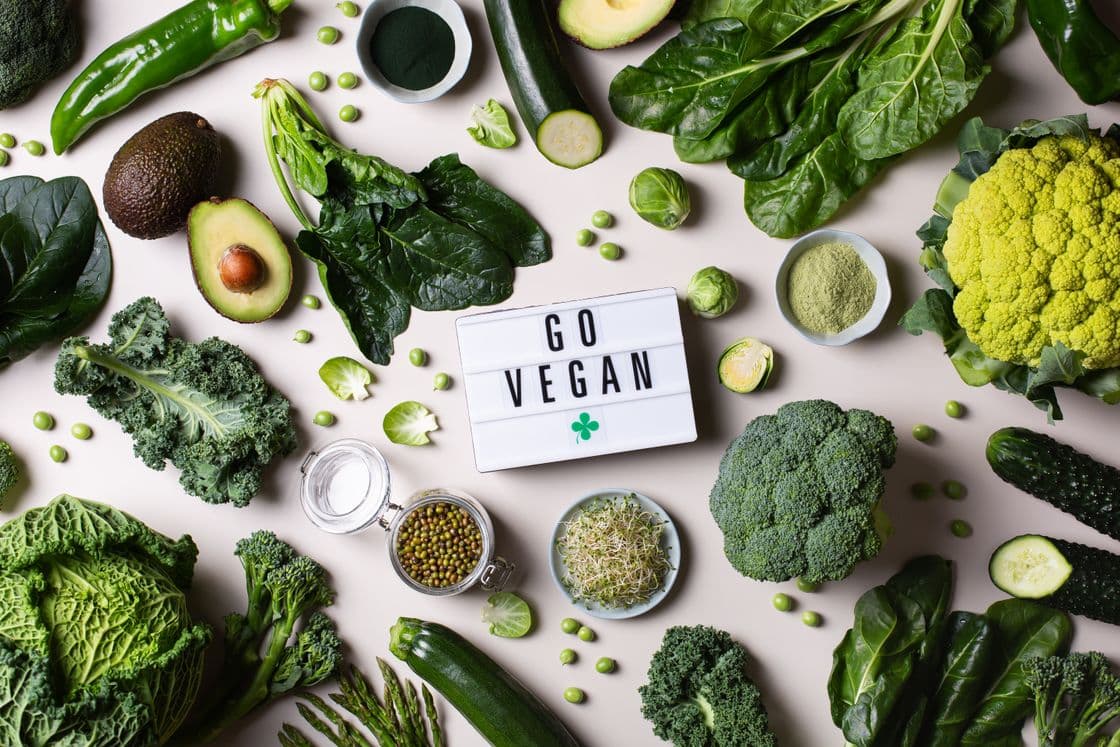 Verschiedene grüne Gemüsesorten und Samen um ein Schild mit der Aufschrift „Go Vegan“ arrangiert.
